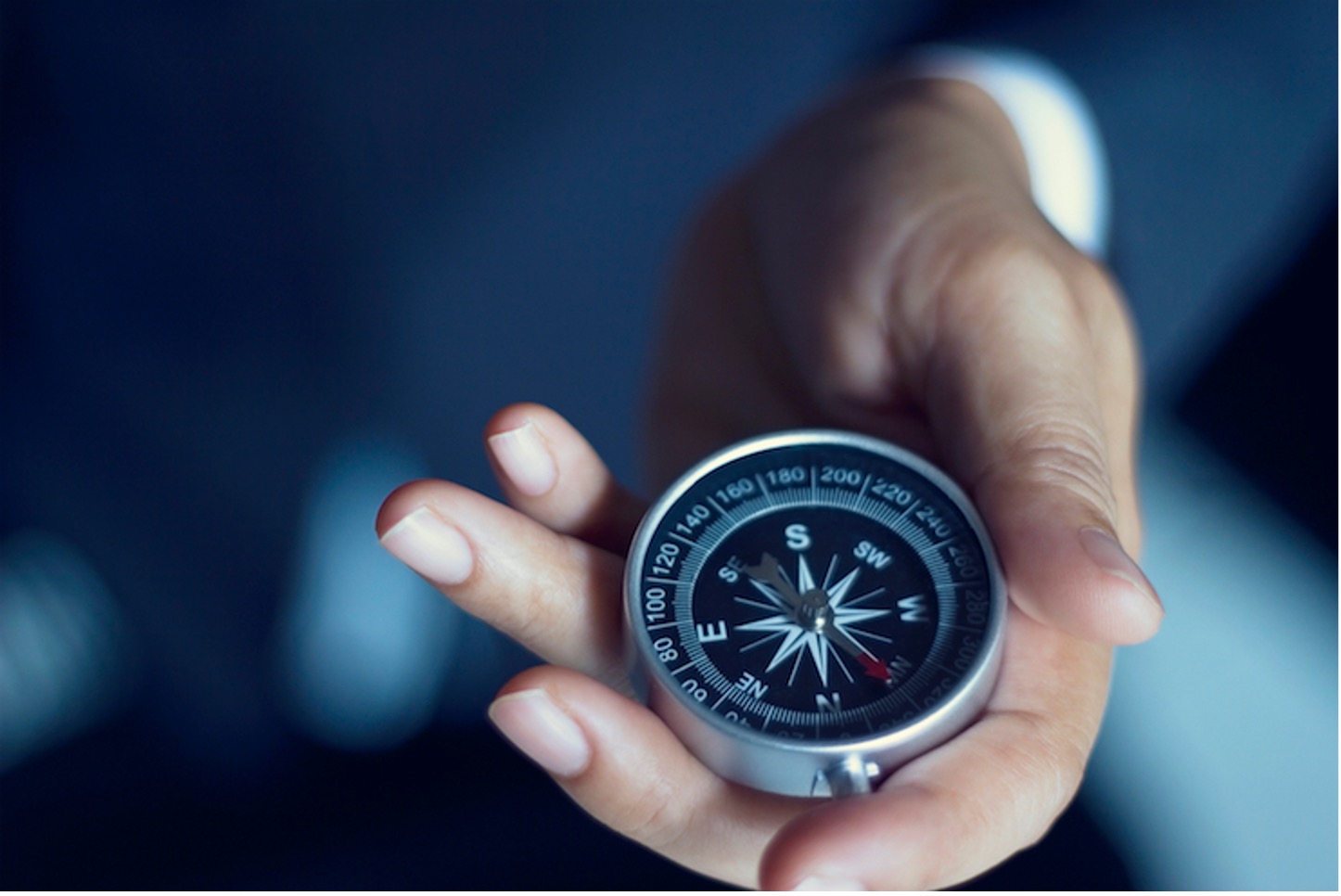 Hand holding a compass against a blue background, symbolizing direction and purpose in employee engagement